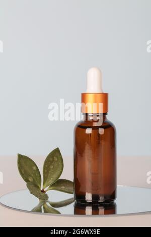 dark amber glass bottle with oil on mirror with green leaf on blue background. copy space. Beauty concept, brand packaging mock up. Stock Photo