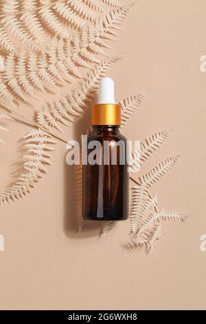 dark amber glass bottle with oil with fern on beige background. Beauty concept, minimalism brand packaging mock up. Stock Photo