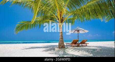 Beautiful tropical island scenery, two sun beds, loungers, umbrella under palm tree. White sand, sea view with horizon, idyllic blue sky, calmness Stock Photo