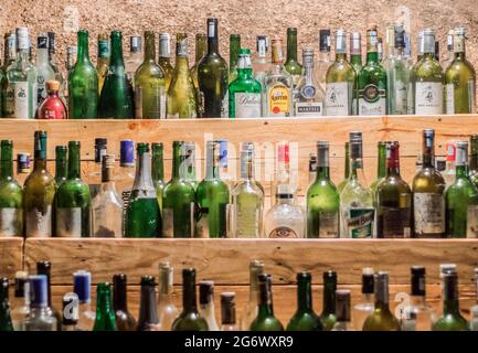 Cam Ranh, Khanh Hoa Province, Vietnam - July 14, 2019: Tops of empty glass bottles of various types of alcohol are visible on three wooden shelves. To Stock Photo