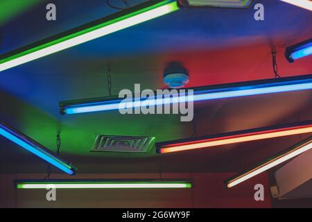 On the ceiling of the room there are fluorescsettingent lamps hanging on chains and burning in different colors. Decoration for the Stock Photo