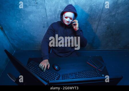 Anonymous hacker wearing face mask working on computer in dark room Stock Photo