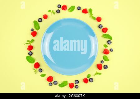 Fresh blueberries, raspberries and mint leaf on top view with blue plate and pastel yellow color background for healthy food concept. Stock Photo