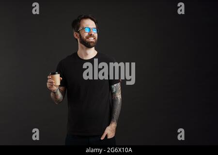 Bearded happy man smiling while drinking coffee takeaway isolated over black background Stock Photo