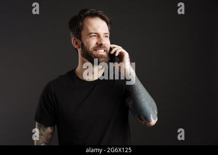 Bearded happy man smiling and talking on cellphone isolated over black background Stock Photo