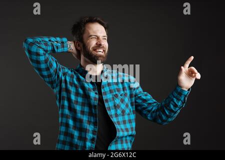 Smiling bearded man pointing finger upward while holding his neck isolated over black background Stock Photo