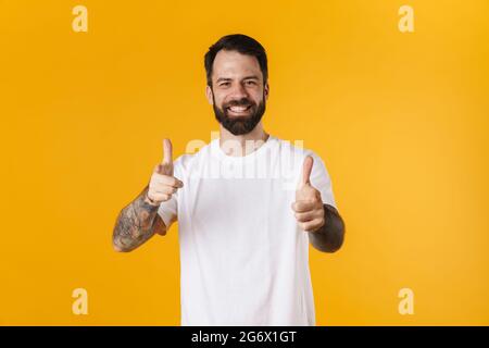 Portrait of a happy brunette bearded man standing over yellow wall, pointing fingers at camera Stock Photo
