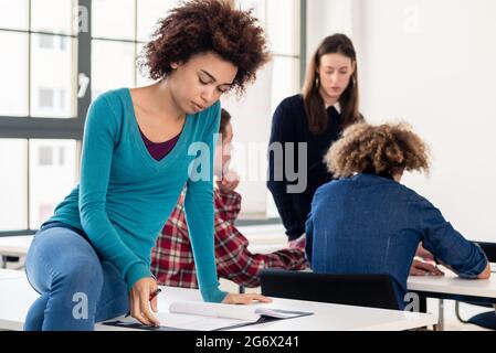 Young African American dedicated student reviewing an essay or course materials while sitting on desk during break at college or university Stock Photo