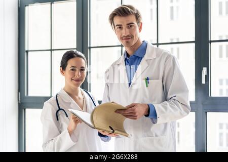 Portrait of two dedicated doctors smiling and looking at camera while holding a tablet and a folder with medical records Stock Photo