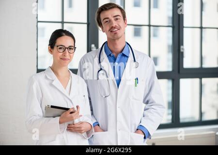 Portrait of two dedicated doctors smiling and looking at camera while holding a tablet and a folder with medical records Stock Photo