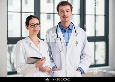 Portrait of two dedicated doctors smiling and looking at camera while holding a tablet and a folder with medical records Stock Photo