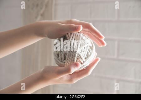 ball of yarn for knitting macrame lies on the hand against the background of a white wall Stock Photo