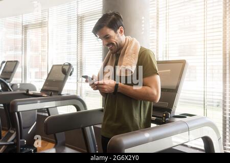 Young handsome man smiling while communicating through text messages on the mobile phone during break at the fitness club Stock Photo