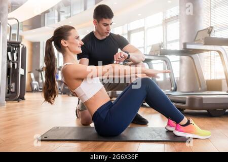 Experienced personal trainer timing and guiding young fit woman