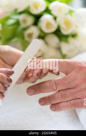 Close-up of the hands of a qualified manicurist filing the nails of a young woman with a white buffer in a trendy nail salon Stock Photo