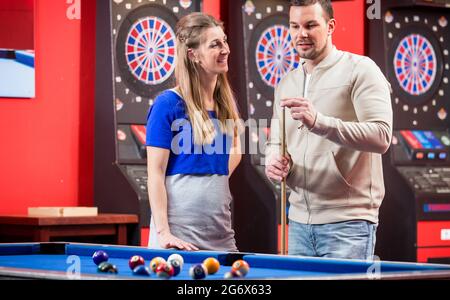 Happy wife looking at husband while playing billiard in club Stock Photo