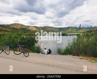 Ankara; Turkey-July 04; 2021: Couple sitting by the lakeside and viewing beautiful view and in Lake Eymir in Ankara. People getting used to new normal Stock Photo