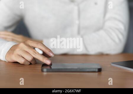 Close up of female using smartphone and holding stylus pen on wooden table with casual clothes Stock Photo