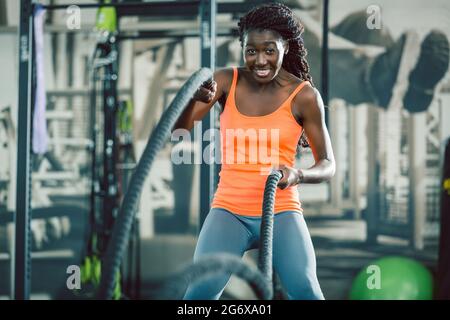 Low-angle view of a strong and beautiful African American woman exercising alternative waves with battle ropes, during functional training workout at Stock Photo