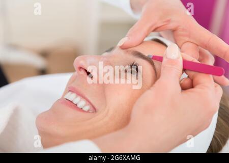 Smiling beautiful woman gets eyebrow correction procedure in salon Stock Photo