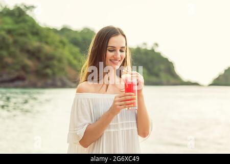 Portrait of a beautiful young woman smiling while holding a fresh watermelon cocktail on a tropical beach during summer vacation in Flores Island, Ind Stock Photo