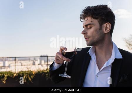 elegant man in suit holding glass of red wine outdoors Stock Photo