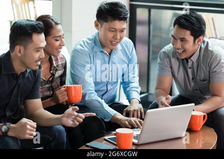 Two cheerful Chinese young men using a laptop while sharing business ideas with their colleagues during work in a successful multinational company Stock Photo