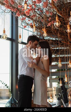 side view of passionate man hugging young brunette woman in restaurant Stock Photo