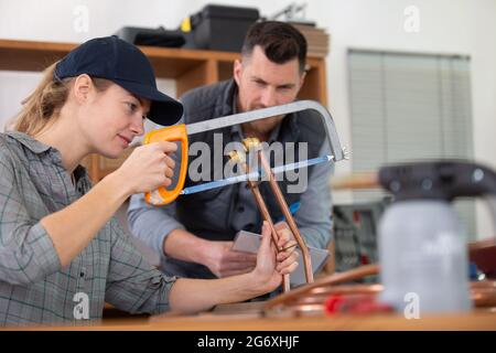 female worker using hacksaw to cut copper pipe Stock Photo