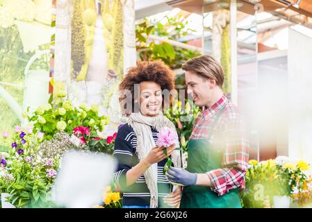 Cheerful Latin American female customer buying flowers at the advice of a helpful and persuasive vendor in a modern flower shop Stock Photo