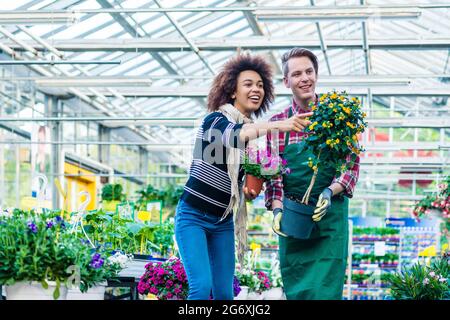 Full length of a handsome and friendly worker helping a female customer with the purchase of an orange decorative houseplant in a modern flower shop Stock Photo