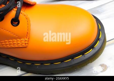 Closeup top view on bright orange color tip of one single leather boot, black sole, yellow stitching on white wood background Stock Photo