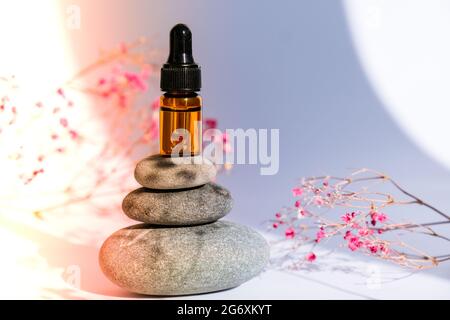 Small bottle of serum on stack of basalt stones on white background. Trendy shadows. Beauty pipette dropper with Gypsophila or baby's breath flowers Stock Photo