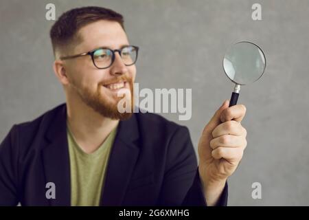 Happy young student or businessman in glasses looking through a magnifying glass Stock Photo