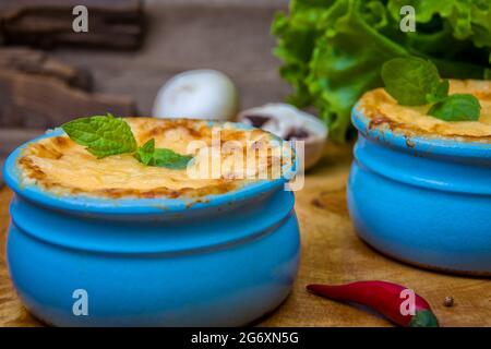 Pots with mushroom julienne on a wooden board, decorated with herbs. Julienne in cocotte with yellow cheese crust. Stock Photo