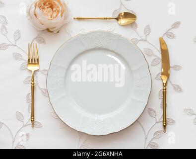 Wedding table arranged with golden cutlery and white charger plate. Mockup for menu, invitation card, festive concept in vintage style Stock Photo