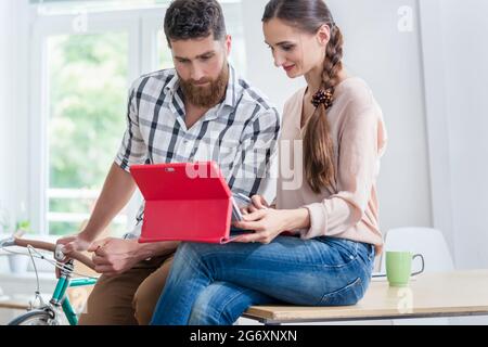 Young female independent worker asking for advice and opinion from her co-worker while using a tablet in a contemporary shared office space Stock Photo