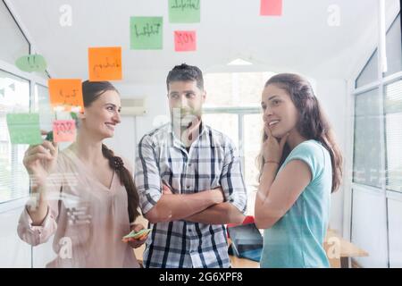 Low-angle view of reliable young workers posting reminders on the transparent wall of an office, next to their colleague in a modern co-working space Stock Photo