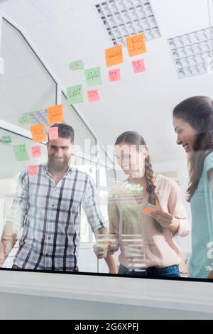 Low-angle view of reliable young workers posting reminders on the transparent wall of an office, next to their colleague in a modern co-working space Stock Photo