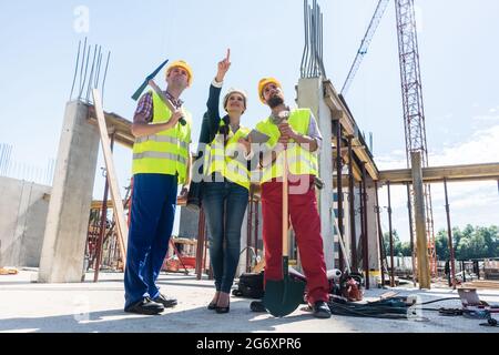 Low-angle view of a visionary architect pointing up while guiding and motivating two workers on the construction site of a new daring project Stock Photo