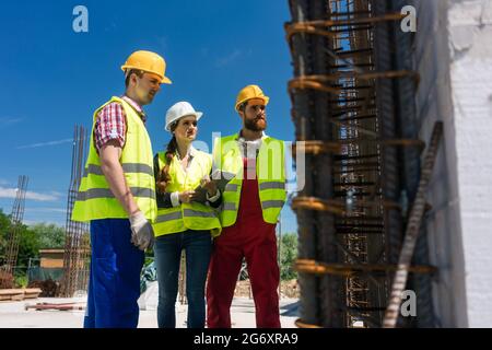 Female manager or architect between two workers supervising the work in progress on the construction site of a building with reinforcing steel structu Stock Photo