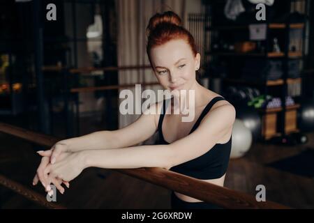 Pretty young red haired woman leaning on ballet barre Stock Photo