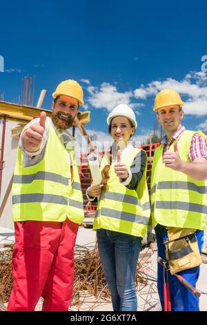 Portrait of three cheerful colleagues in a construction team, looking at camera while showing thumbs up as a gesture of agreement and confidence durin Stock Photo