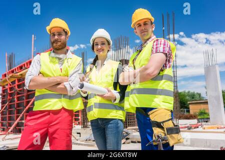 Portrait of three confident and reliable young employees, a female architect and two blue-collar workers, looking at camera while posing on the constr Stock Photo