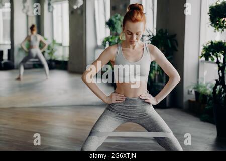 Slender sportıve redhead lady performing sit ups with fitness elastic band Stock Photo