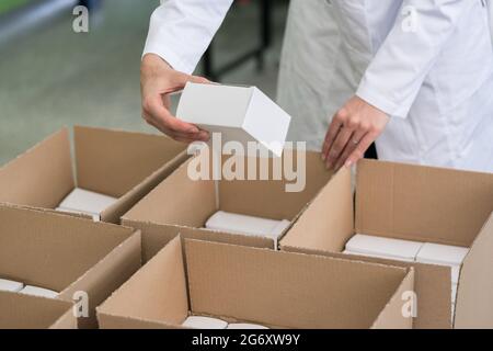 High-angle close-up view of the hands of a manufacturing worker putting packed products in cardboard boxes, before export or shipping during manual wo Stock Photo
