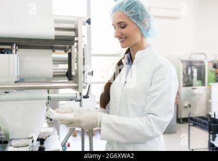 Side view of a happy manufacturing employee wearing white lab coat, protective headwear and gloves while handling sterile wipes in a contemporary cosm Stock Photo