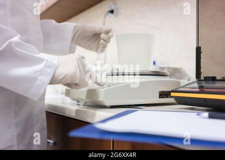 Side view close-up of the hands of an expert in chemical substances, analyzing liquid sample with modern equipment in the laboratory of a cosmetics fa Stock Photo