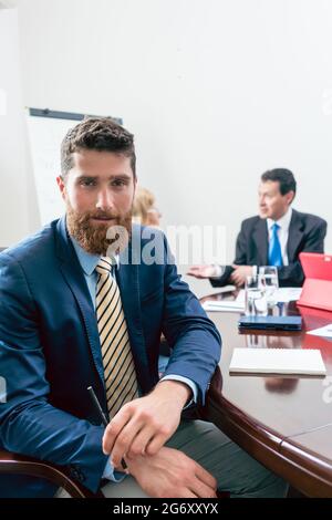 Portrait of a handsome young businessman wearing elegant formal suit, while looking at camera with confidence during a meeting in the conference room Stock Photo
