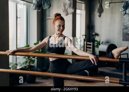 Happy young woman good stretch posing in fitness studio during barre workout Stock Photo